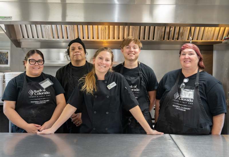 Five people standing in a kitchen in black uniforms