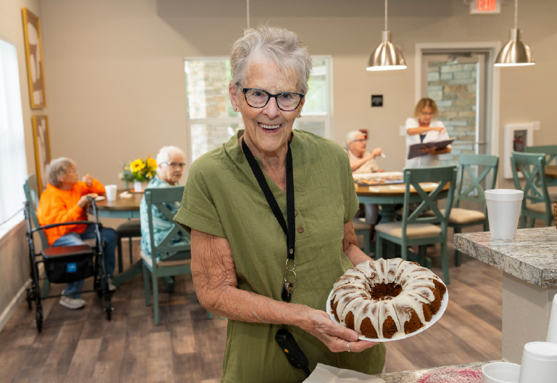 A woman holding a cake in front of a table of people.