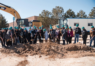 a large group of people in hardhats and holding shovels at a groundbreaking