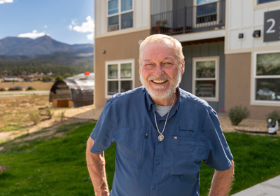 A man with white hair and a blue shirt standing outside a multifamily building