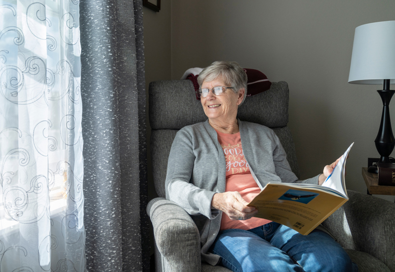 Salida Ridge apartments female resident sitting a chair holding a magazine and looking out a window