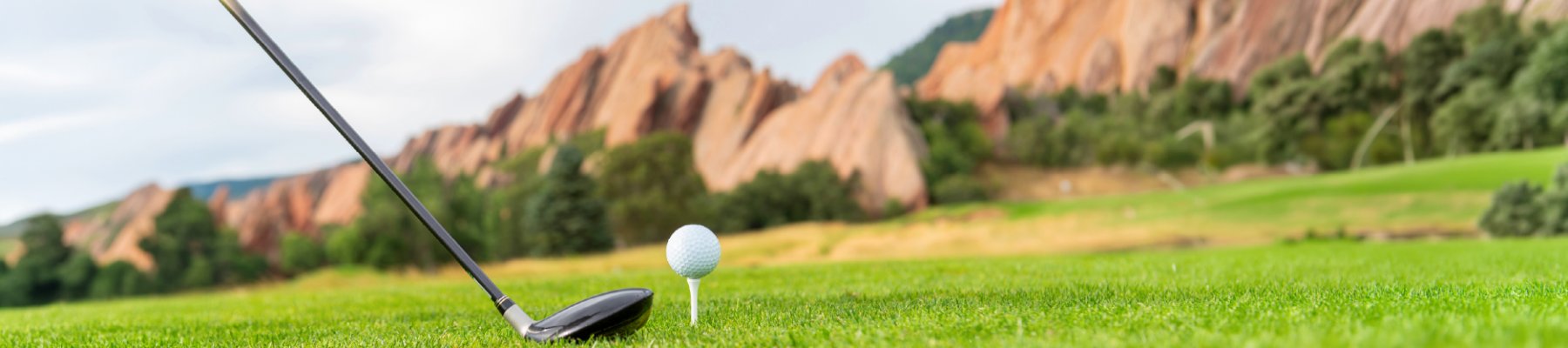 A golf club hitting a golf ball in front of red rocks
