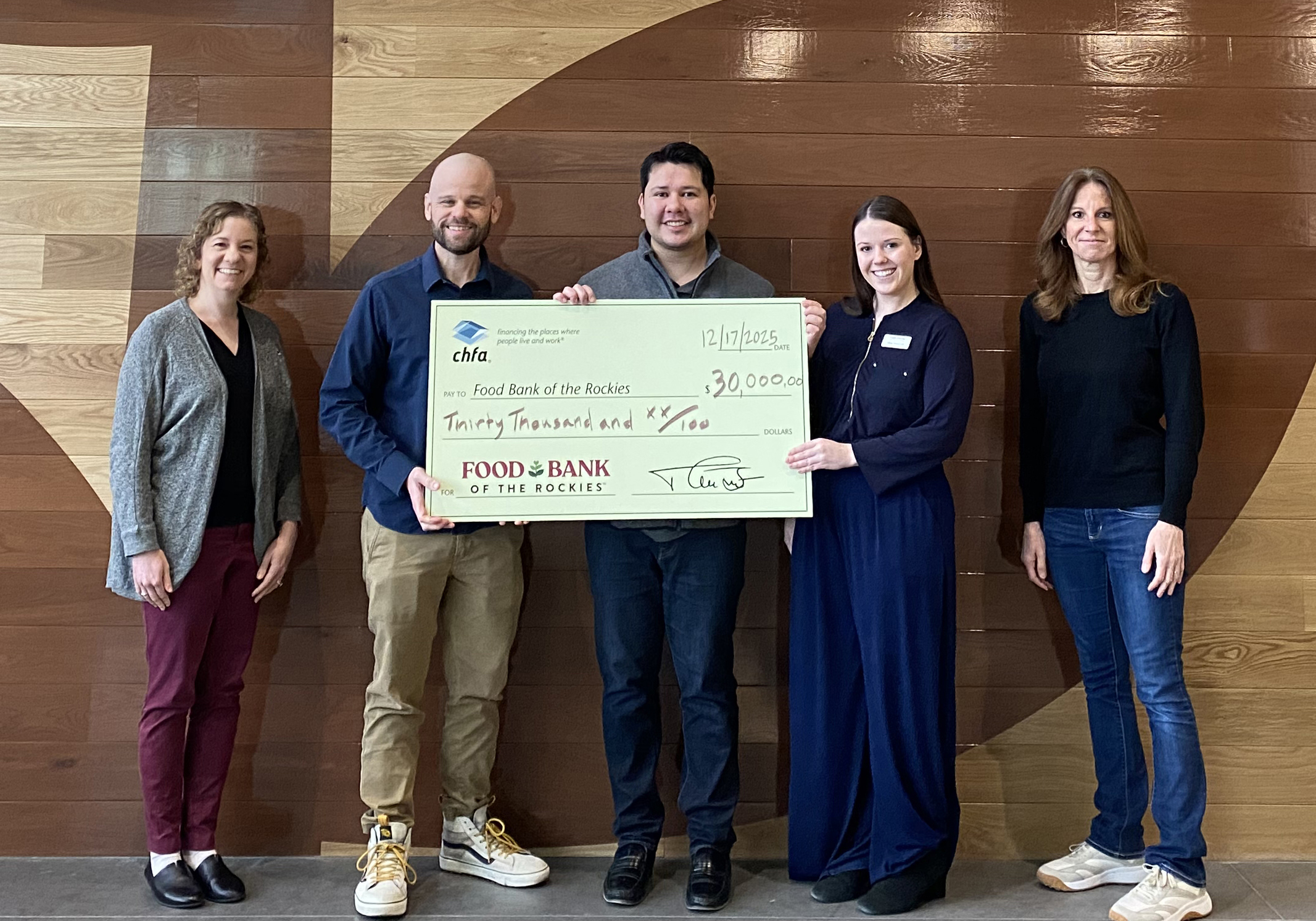 Five people standing against a wood wall holding a large check for Food Bank of the Rockies. 
