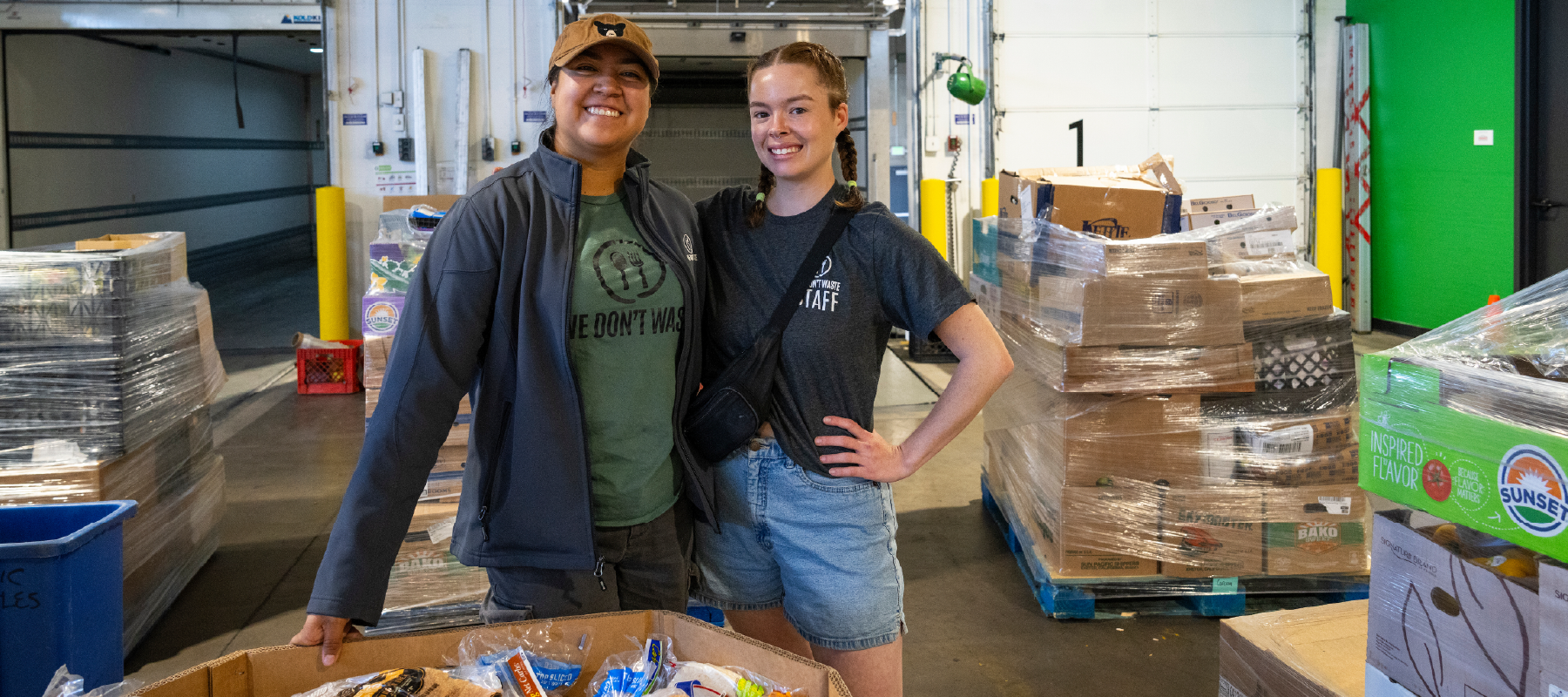 Two people standing around pallets of food in a warehouse