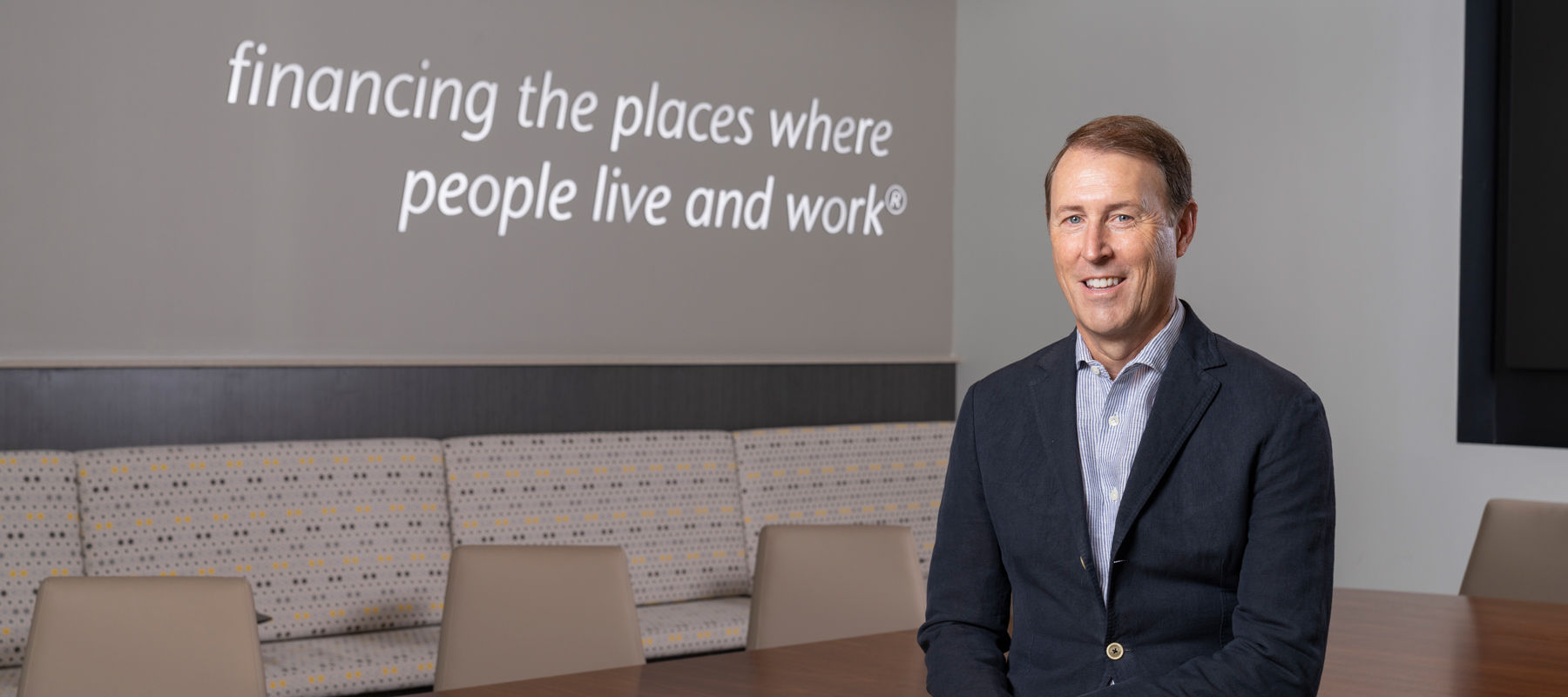 Cris White sitting in conference room with "financing the places people live and work" posted on the wall behind him