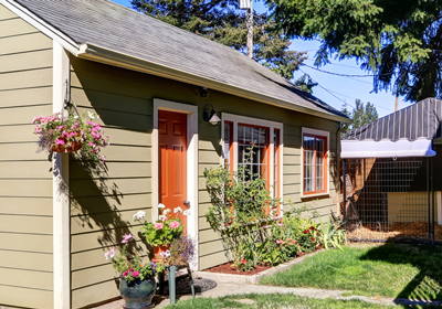 A tan ADU with a red door and plants out front.