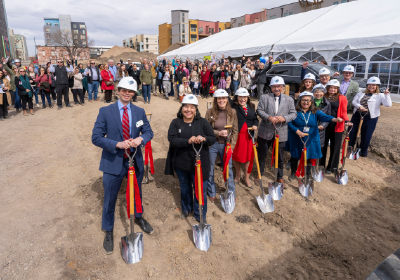 A group of people in hardhats holding shovels on bare ground