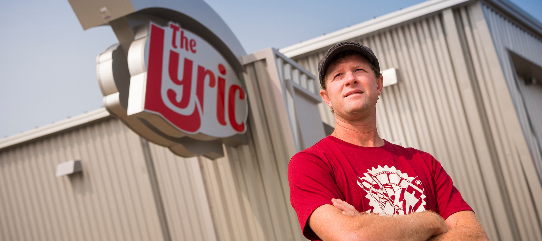 A person in a red tshirt standing in front of a building with a sign that reads the Lyric