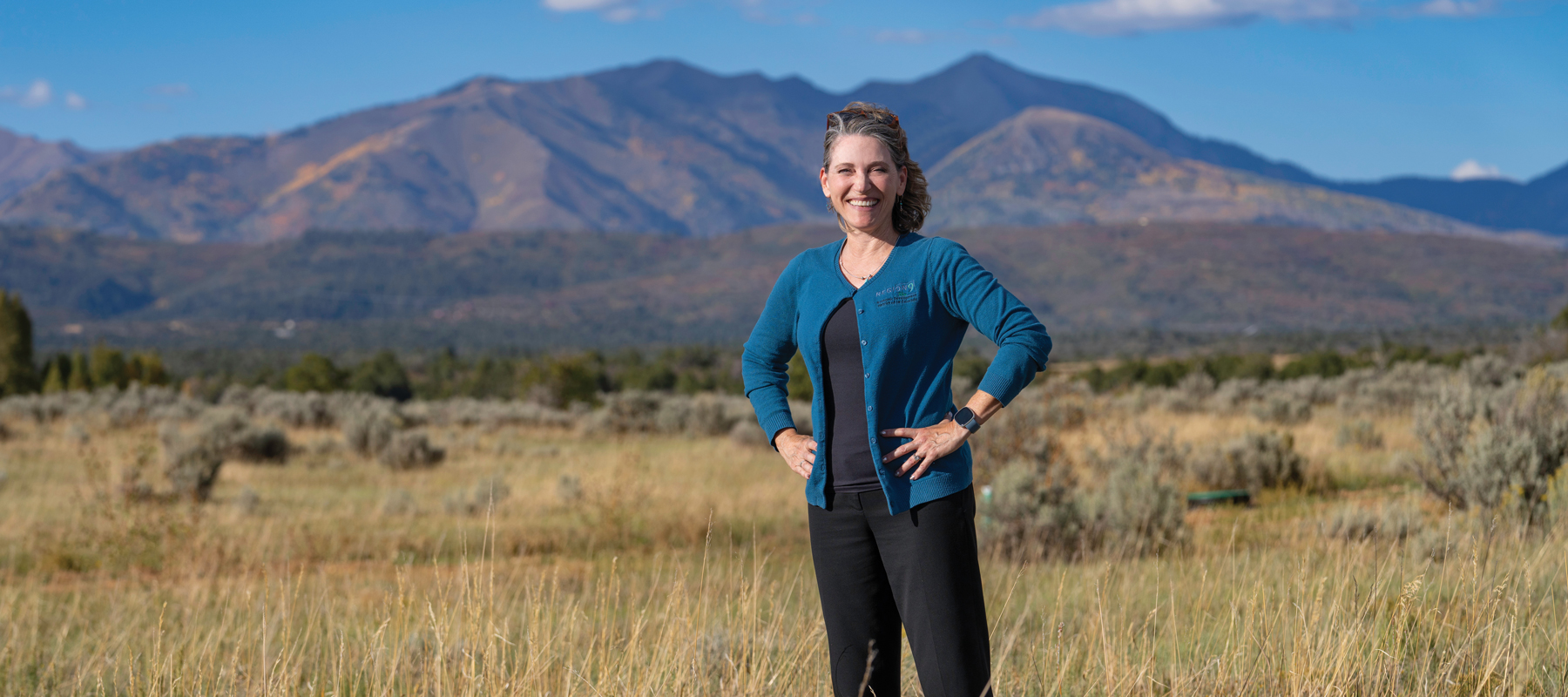 Laura Lewis Marchino standing in a field with mountains in the background